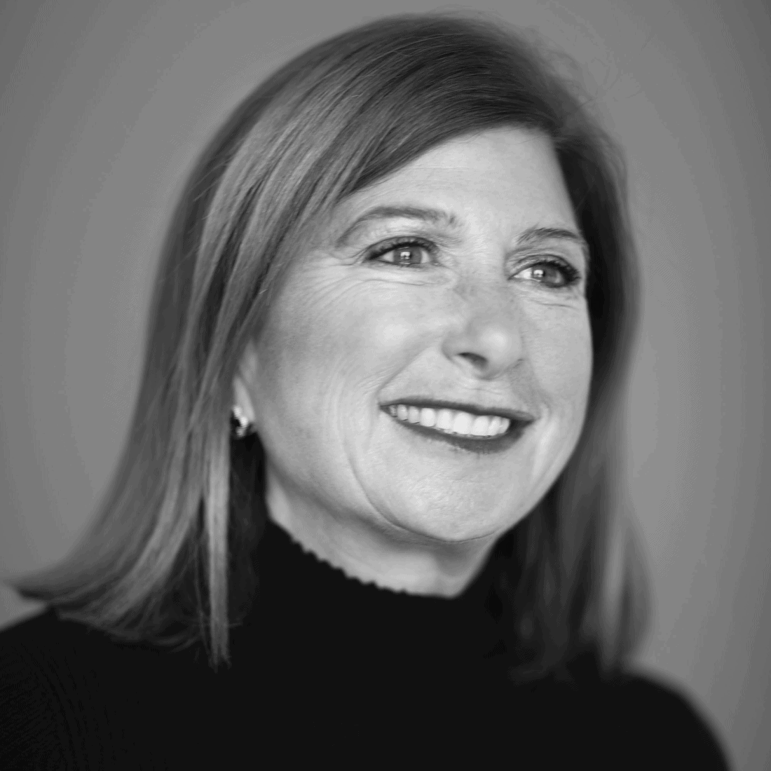 Black and white portrait of a woman with shoulder-length hair, smiling and looking slightly to her right. She is wearing a dark turtleneck sweater. The background is blurred, directing focus to her face—a distinguished member of The Representation Project's Board of Directors.
