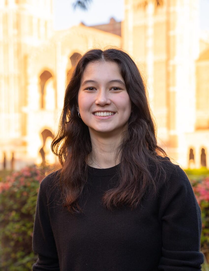 Hayley Labia, a member of The Representation Project's Youth Advisory Council, smiles while standing in front of a building with bushes in the foreground.