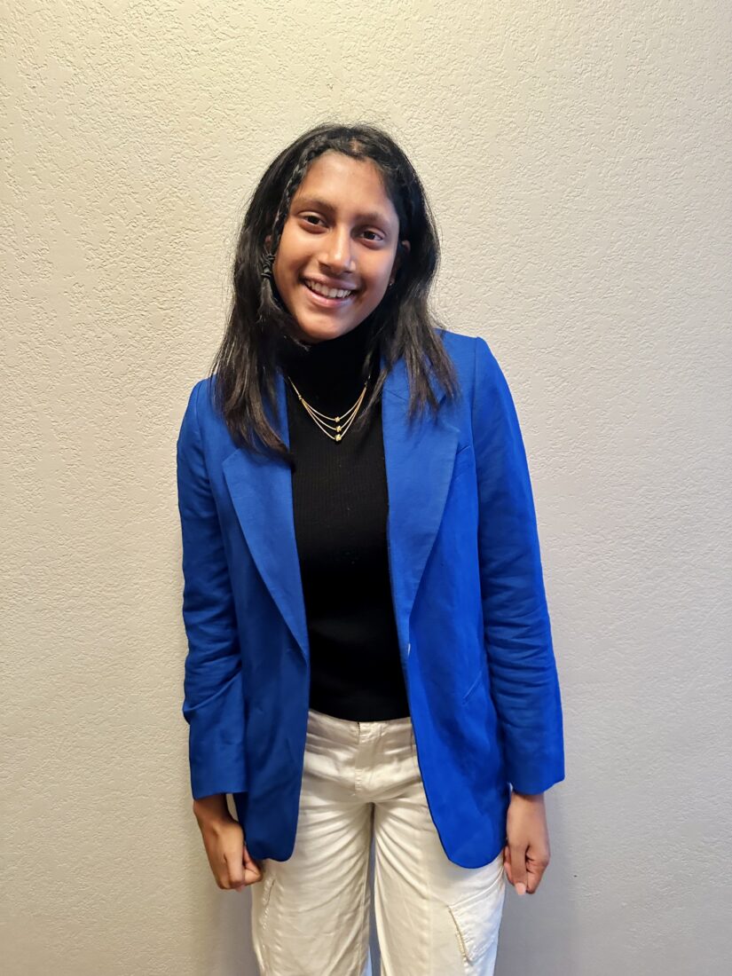 Janvi Sahasra Niranjan, a member of The Representation Project's Youth Advisory Council, smiles while standing against a light-colored wall.