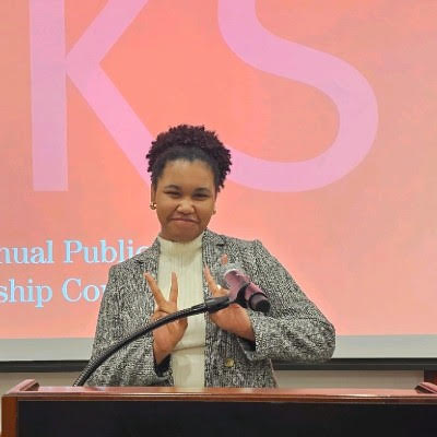 Love Adu, a member of The Representation Project's Youth Advisory Council stands at a podium making a peace sign with both hands.