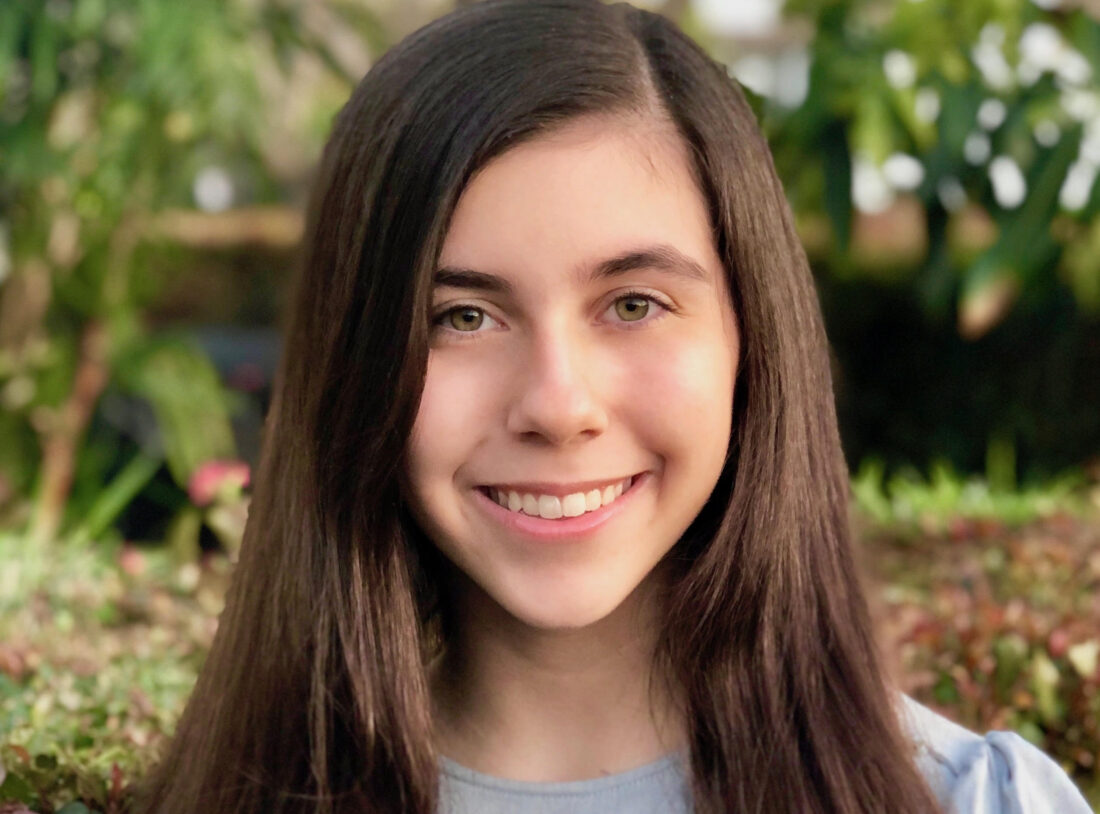 Noelle Hardy, a member of The Representation Project's Youth Advisory Council, smiles outdoors against a backdrop of blurred greenery.