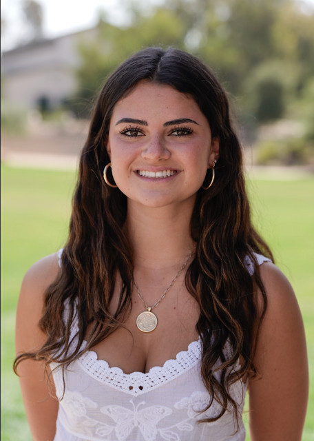 Sienna Charvel, a member of The Representation Project's Youth Advisory Council, smiles at the camera against a blurred backdrop of outdoor greenery.