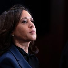 Profile of Kamala Harris against a black background. She wears a navy and black suit.