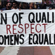 Men marching in allyship with women. Several men hold up a sign together: "Men of Quality Respect Women's Equality"