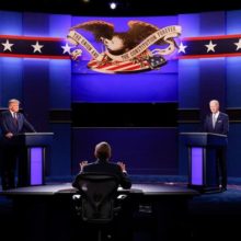 Still from presidential debate. Trump at the left podium, Biden at the right podium. A moderator is seated between them at the front of the stage.
