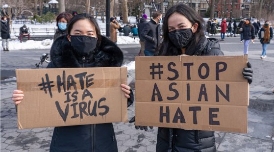 Two women in winter coats and face masks at a Stop Asian Hate rally, holding up signs.