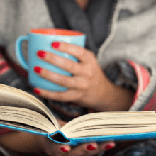 Person in covers, reading with a mug in hand