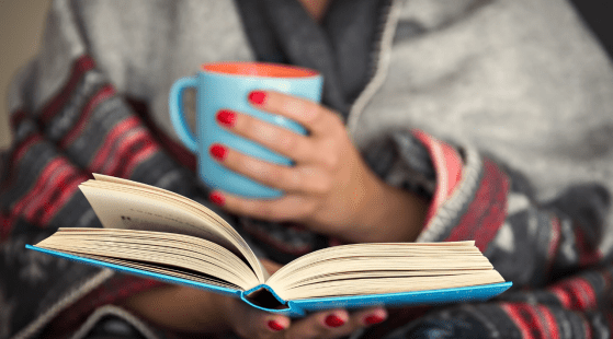 Person in covers, reading with a mug in hand