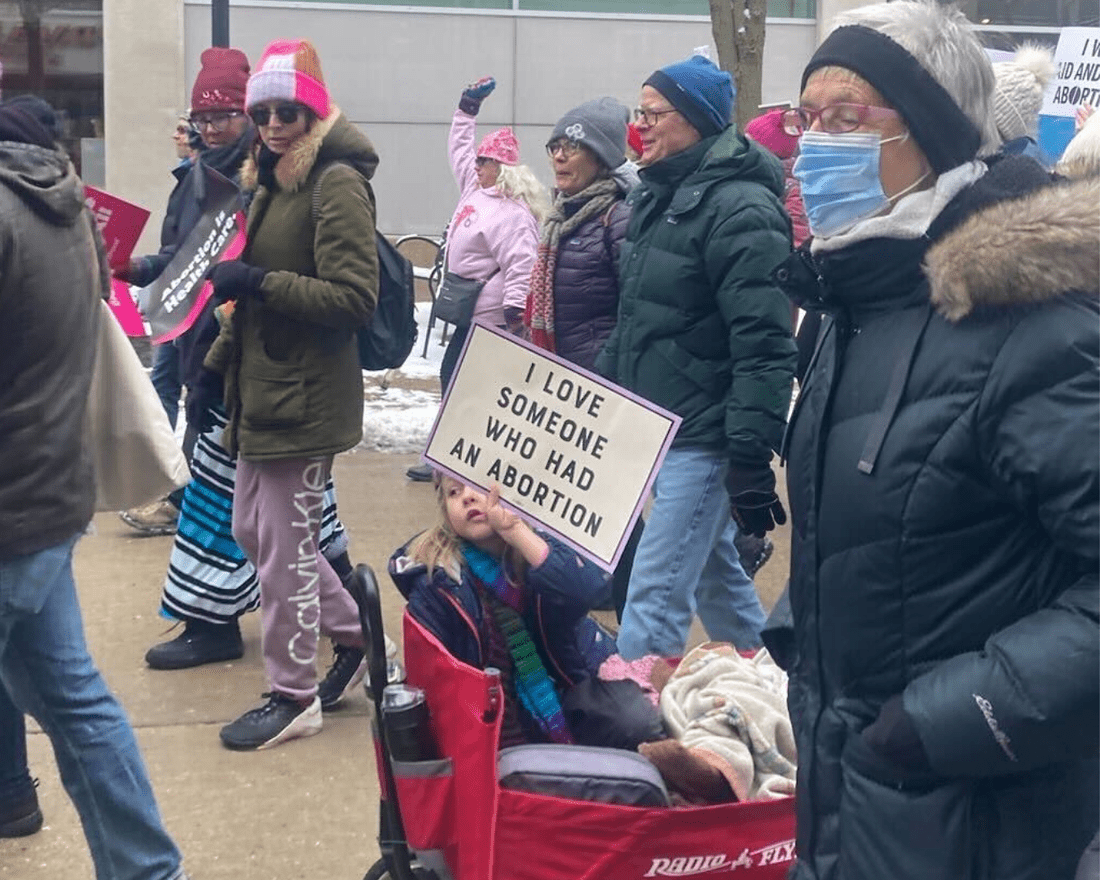 A girl sits in a fabric wagon holding a "I love someone who had an abortion" sign.