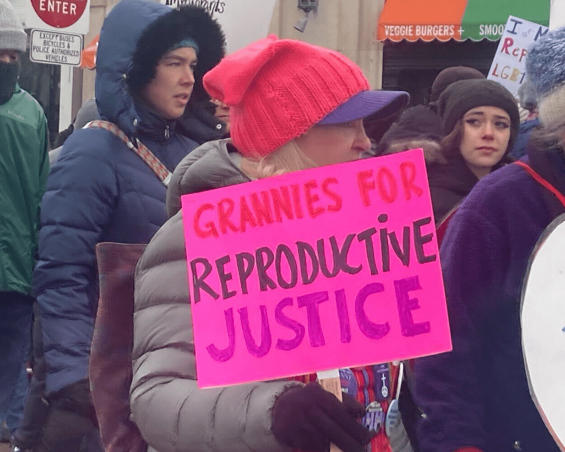 A woman holds a pink "Grannies for Reproductive Justice" sign